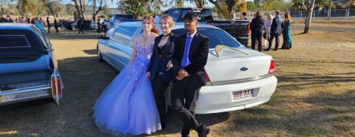 Three well-dressed youth standing in front of our 9 seater Limo at a school formal in 2023.